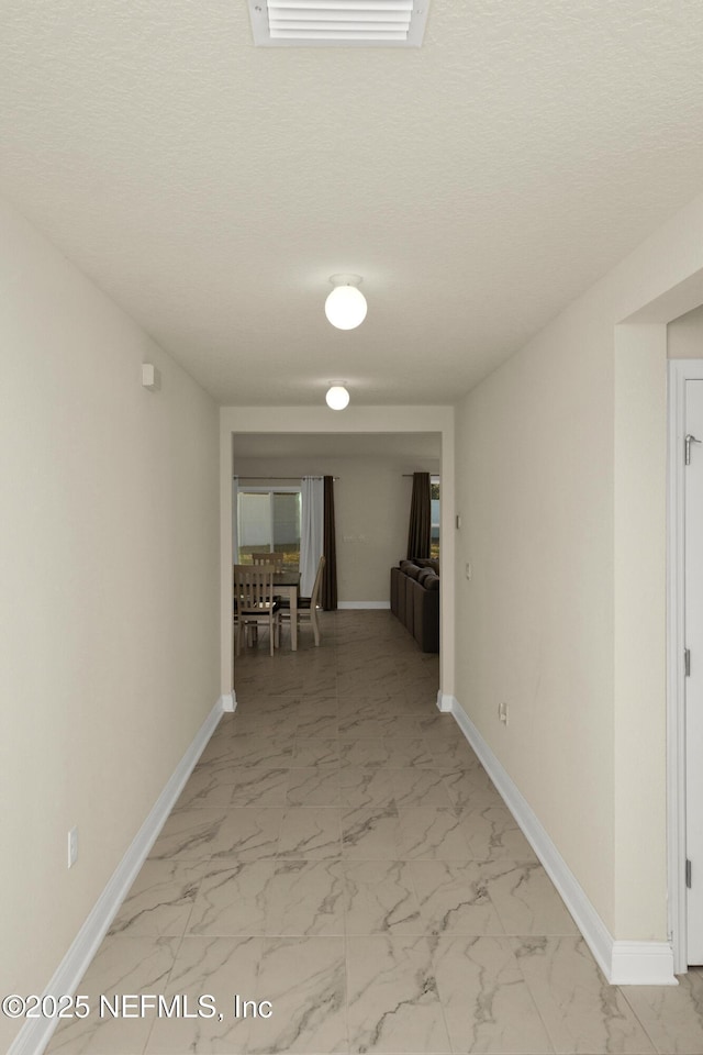 corridor with visible vents, marble finish floor, a textured ceiling, and baseboards