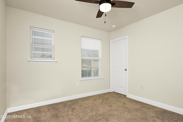 carpeted spare room with a ceiling fan and baseboards