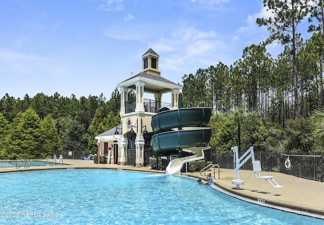 pool with a patio area, a water slide, and fence