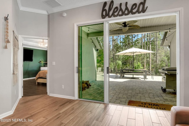 doorway with a ceiling fan, wood finished floors, visible vents, baseboards, and crown molding