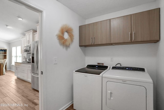 laundry area with washing machine and dryer, cabinet space, light wood-style floors, crown molding, and baseboards