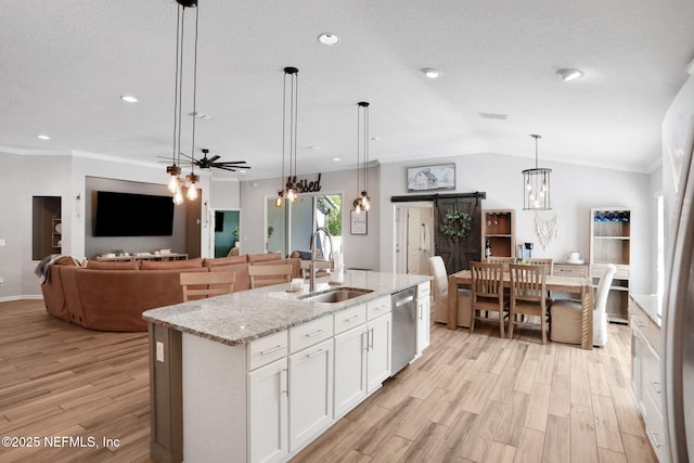 kitchen featuring light wood finished floors, a sink, vaulted ceiling, dishwasher, and a barn door