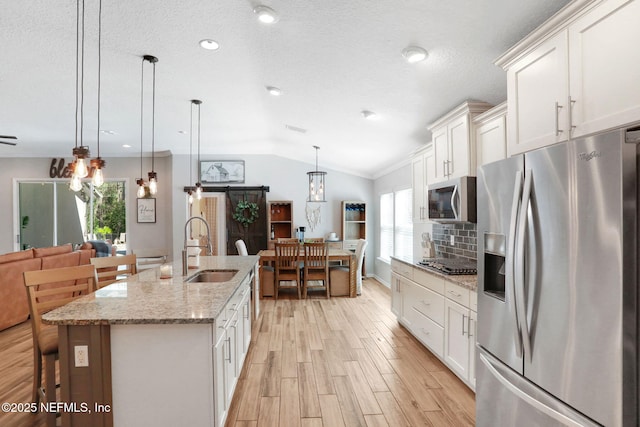 kitchen featuring light wood-type flooring, vaulted ceiling, white cabinets, stainless steel appliances, and a sink