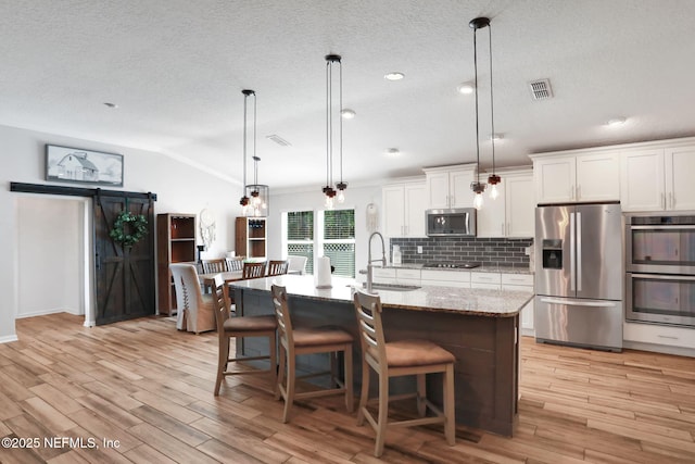 kitchen with visible vents, a sink, stainless steel appliances, vaulted ceiling, and backsplash