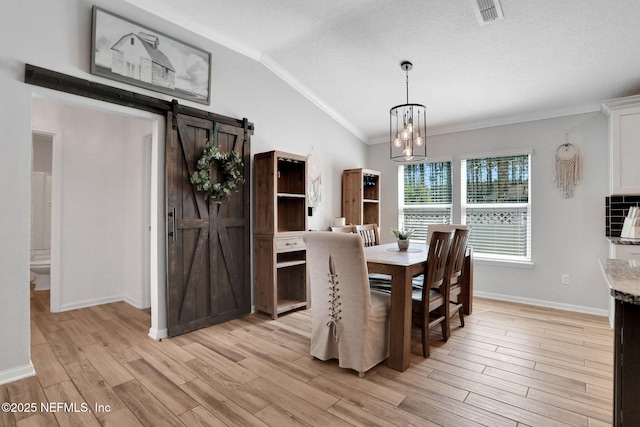 dining room with visible vents, light wood-style flooring, ornamental molding, a barn door, and a chandelier