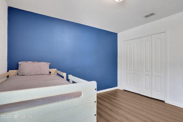 bedroom featuring visible vents, a textured ceiling, baseboards, and wood finished floors