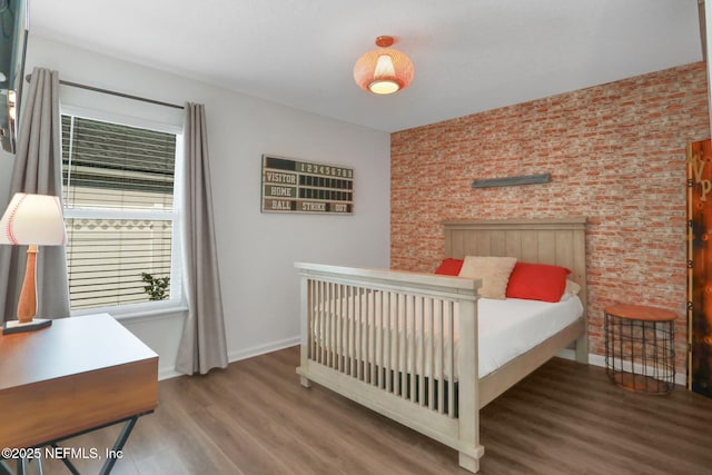 bedroom featuring wood finished floors, baseboards, and brick wall