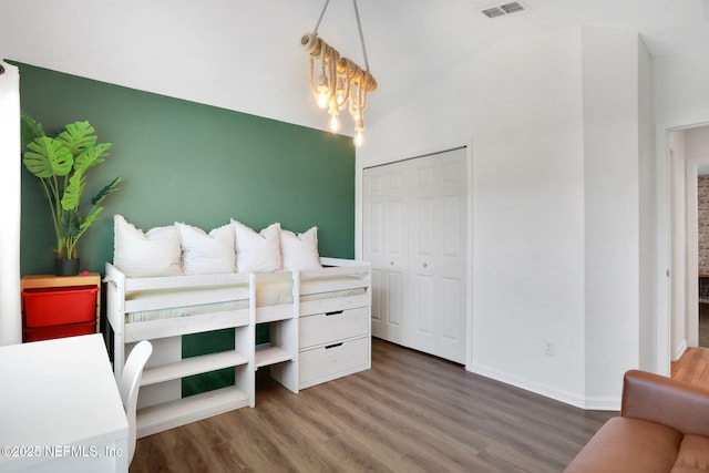 bedroom featuring wood finished floors, visible vents, baseboards, vaulted ceiling, and a closet