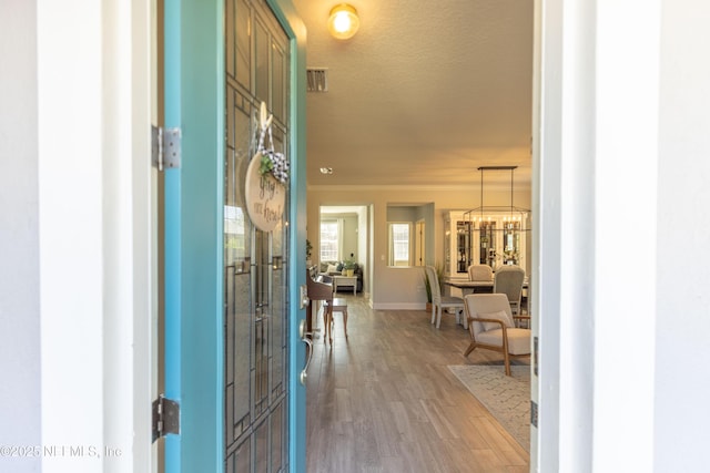 entryway with baseboards, ornamental molding, light wood-style floors, a textured ceiling, and a chandelier