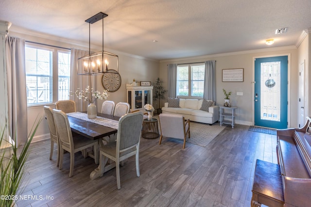 dining area with dark wood-type flooring, a notable chandelier, visible vents, and ornamental molding