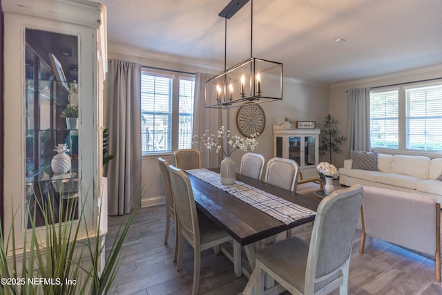 dining area with a wealth of natural light, an inviting chandelier, wood finished floors, and crown molding