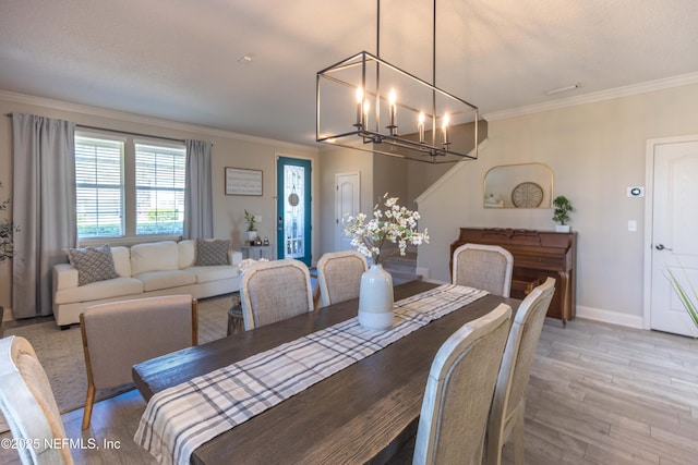 dining area featuring light wood-style floors, baseboards, a notable chandelier, and ornamental molding