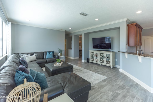 living area with visible vents, baseboards, ornamental molding, recessed lighting, and light wood-style flooring