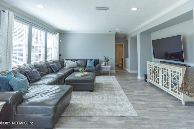 living area featuring wood finished floors, visible vents, baseboards, ornamental molding, and a textured ceiling