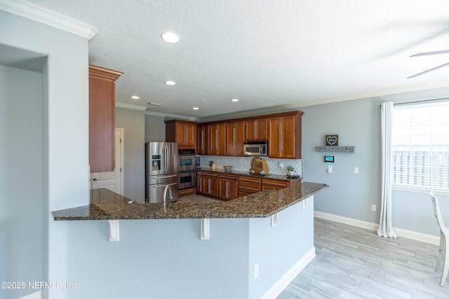 kitchen with backsplash, a breakfast bar, dark stone counters, a peninsula, and appliances with stainless steel finishes