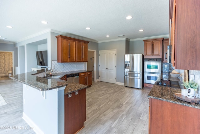 kitchen with a sink, dark stone counters, appliances with stainless steel finishes, and a peninsula