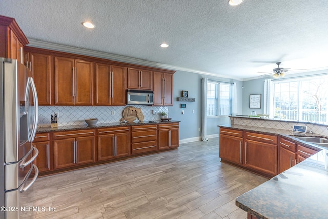 kitchen with tasteful backsplash, ornamental molding, light wood-style flooring, brown cabinetry, and stainless steel appliances