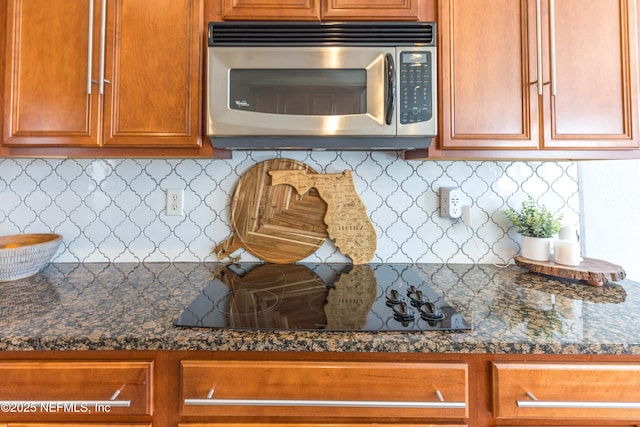 kitchen featuring brown cabinetry, dark countertops, decorative backsplash, stainless steel microwave, and black electric cooktop