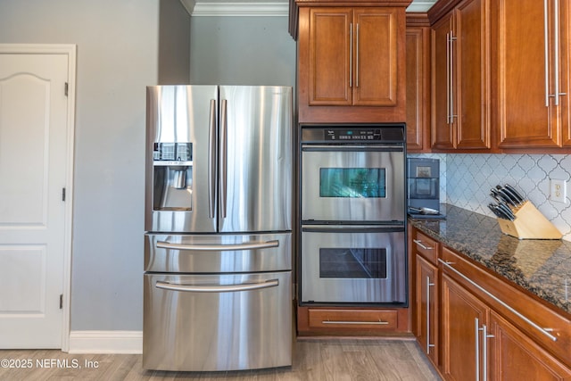 kitchen featuring brown cabinetry, dark stone countertops, appliances with stainless steel finishes, and light wood-style flooring