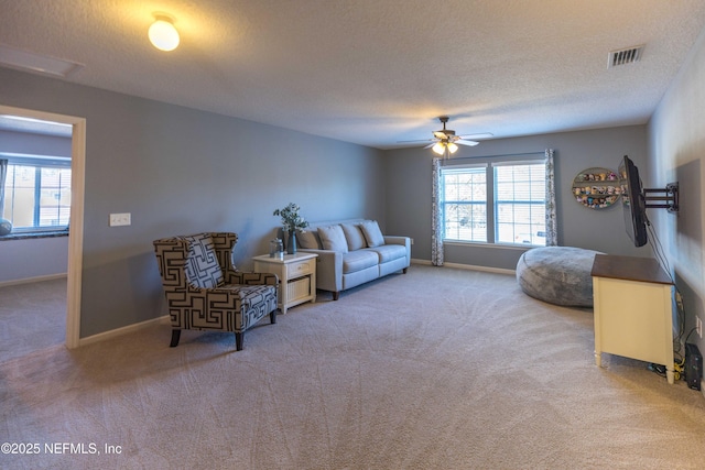 carpeted living area featuring visible vents, plenty of natural light, a textured ceiling, and a ceiling fan