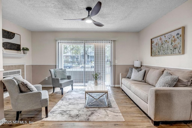 living room with a fireplace, a textured ceiling, light wood-style floors, and a ceiling fan