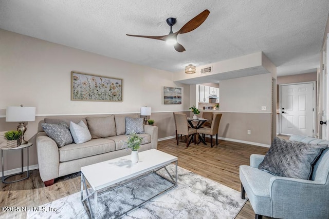 living room with a textured ceiling, light wood-style floors, visible vents, and ceiling fan