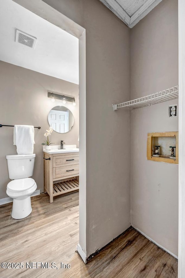 half bath with visible vents, toilet, wood finished floors, and vanity