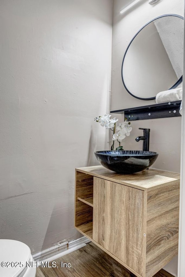 half bathroom with toilet, wood finished floors, and vanity