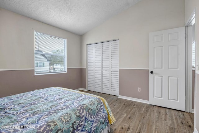 bedroom with a textured ceiling, wood finished floors, a closet, baseboards, and vaulted ceiling