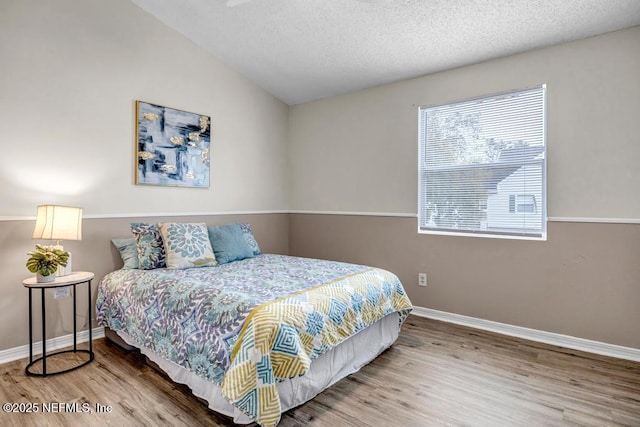 bedroom with vaulted ceiling, a textured ceiling, baseboards, and wood finished floors