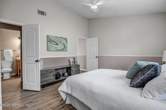 bedroom with ceiling fan, visible vents, wood finished floors, and vaulted ceiling