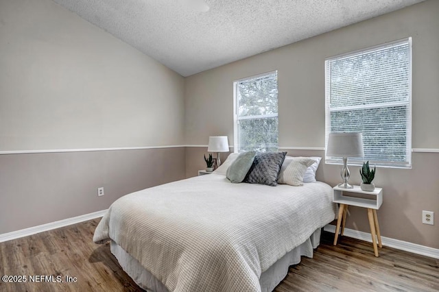 bedroom with a textured ceiling, baseboards, and wood finished floors