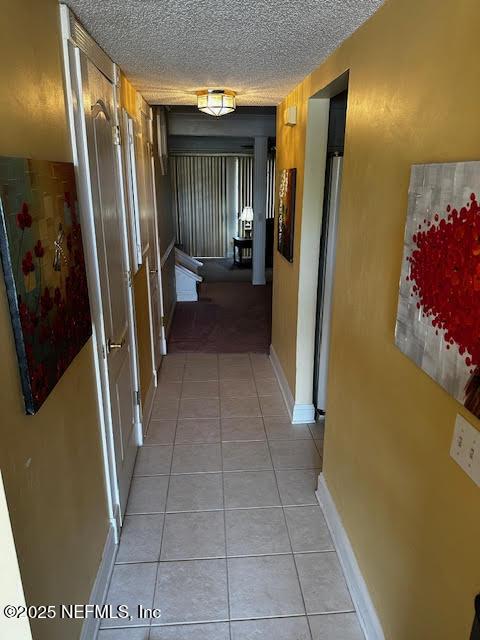 hallway featuring light tile patterned floors, baseboards, and a textured ceiling