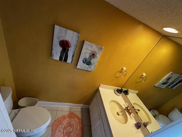 bathroom featuring toilet, a textured ceiling, tile patterned flooring, baseboards, and vanity