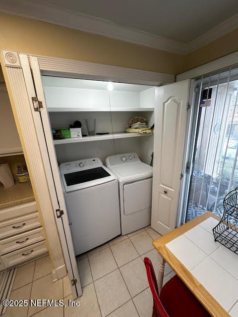 clothes washing area with washing machine and clothes dryer, laundry area, crown molding, and light tile patterned floors