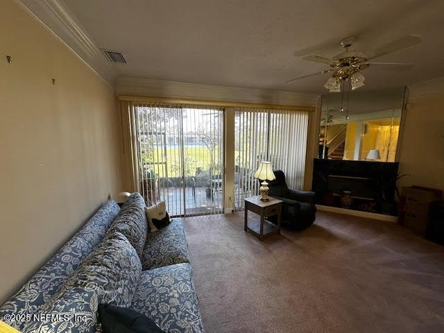 living area featuring visible vents, crown molding, a ceiling fan, and carpet floors