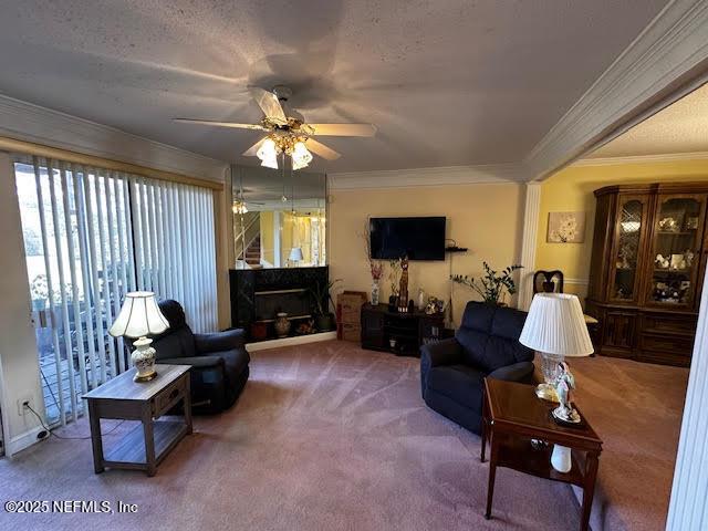 carpeted living area with a ceiling fan, a textured ceiling, a fireplace, and ornamental molding