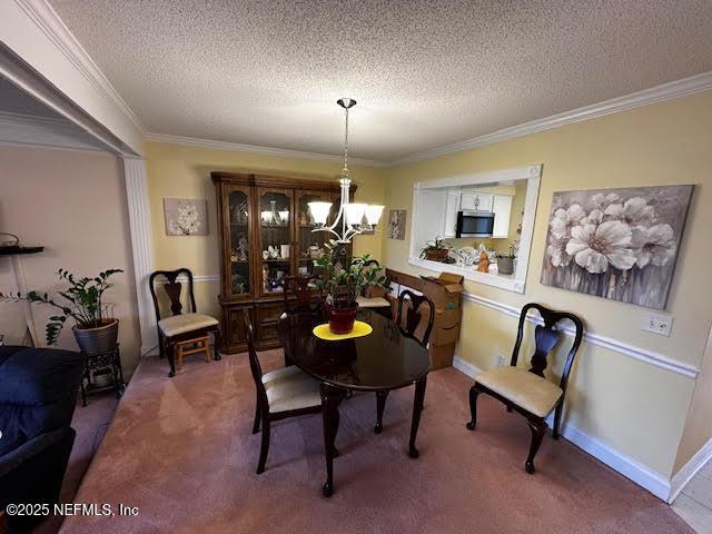 dining room with carpet flooring, a textured ceiling, an inviting chandelier, and ornamental molding