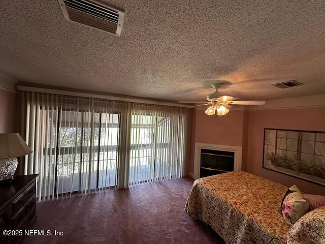 carpeted bedroom featuring visible vents, a textured ceiling, and a glass covered fireplace