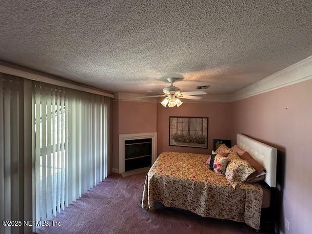 carpeted bedroom featuring visible vents, a textured ceiling, a fireplace, crown molding, and ceiling fan