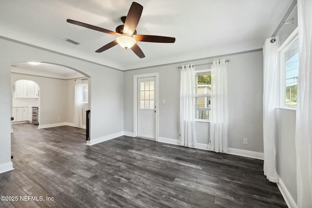 empty room featuring a ceiling fan, dark wood-style floors, visible vents, baseboards, and arched walkways