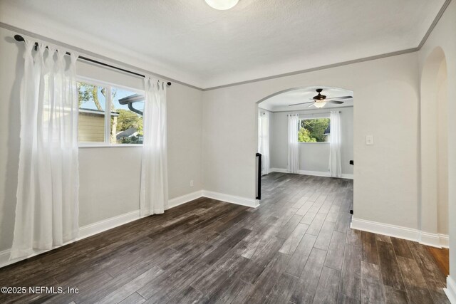 unfurnished room with dark wood-type flooring, crown molding, baseboards, and arched walkways