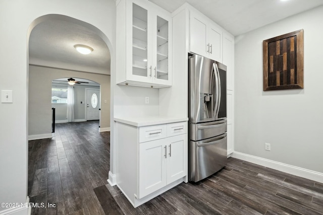 kitchen featuring glass insert cabinets, stainless steel fridge with ice dispenser, light countertops, arched walkways, and white cabinets