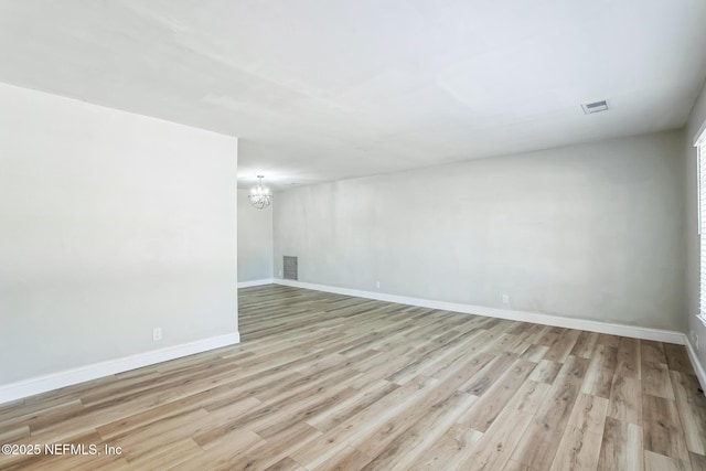 spare room with visible vents, baseboards, light wood-style floors, and a chandelier