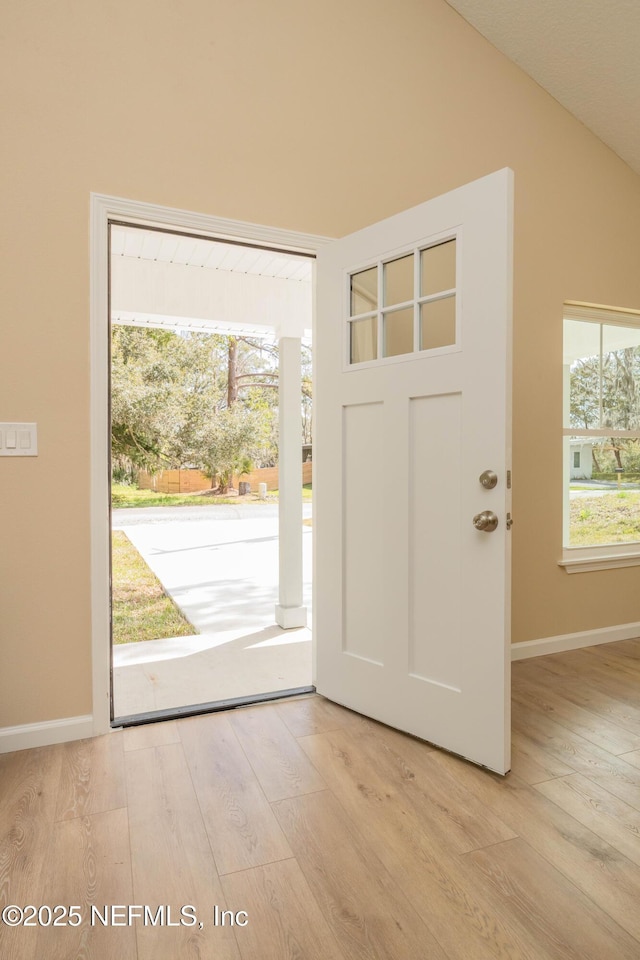 entrance foyer featuring light wood-type flooring, lofted ceiling, and baseboards