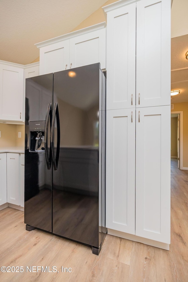 kitchen featuring light countertops, white cabinets, black fridge with ice dispenser, and light wood finished floors