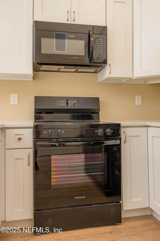 kitchen with light wood finished floors, white cabinetry, black appliances, and light countertops