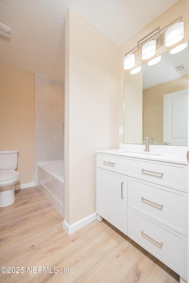 bathroom featuring visible vents, baseboards, toilet, wood finished floors, and vanity