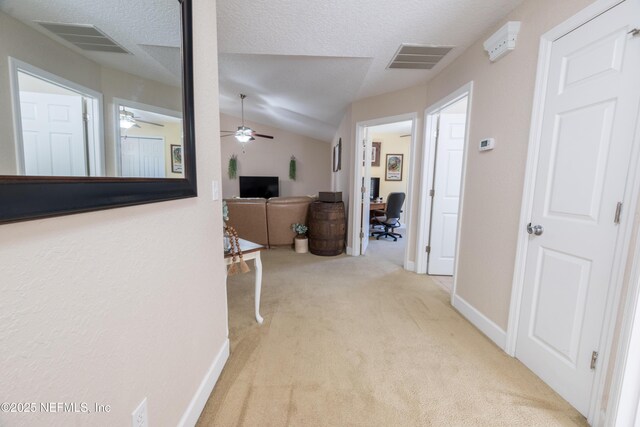 hallway with vaulted ceiling, visible vents, carpet floors, and a textured ceiling