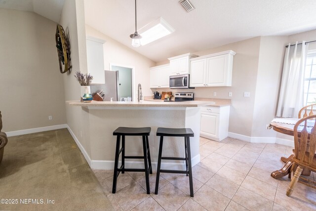 kitchen with visible vents, lofted ceiling, stainless steel appliances, light countertops, and a kitchen bar